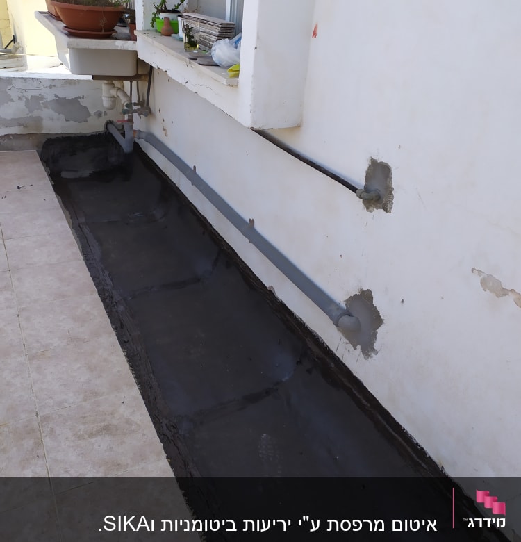 איטום גג עם חומר שחור ליד קיר לבן